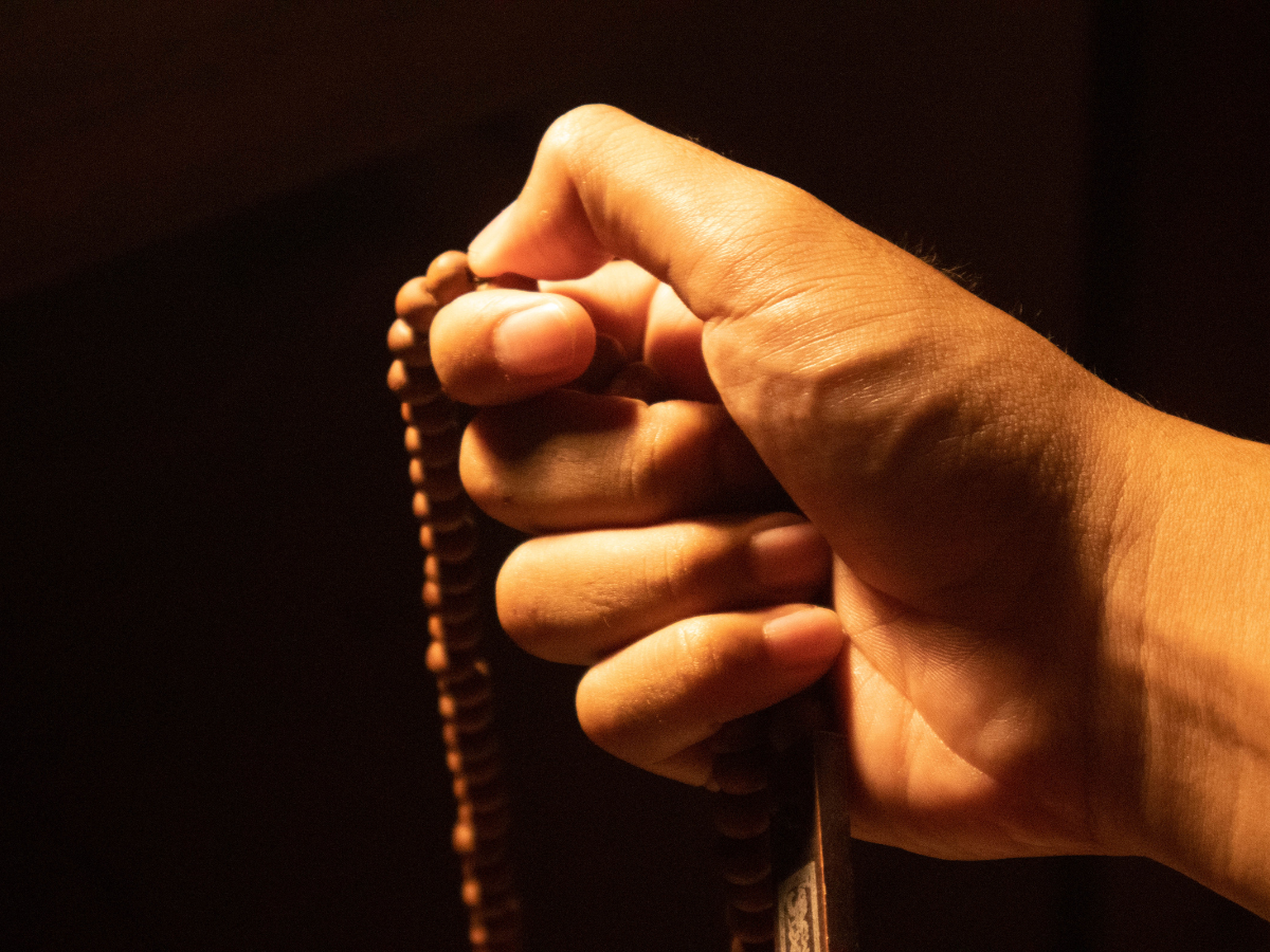 Close-up of a hand holding a tasbeeh (prayer beads), emphasizing the textured beads and the person's focused grip